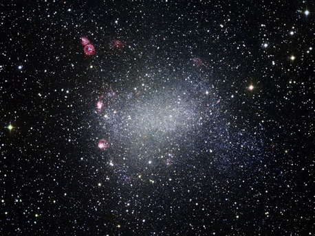 this dwarf irregular galaxy is one of the Milky Way’s galactic neighbors. The dwarf galaxy has no shortage of stellar splendor and pyrotechnics. Reddish nebulae in this image reveal regions of active star formation, wherein young, hot stars heat up nearby gas clouds. Also prominent in the upper left of this new image is a striking bubble-shaped nebula. At the nebula’s center, a clutch of massive, scorching stars send waves of matter smashing into surrounding interstellar material, generating a glowing structure that appears ring-like from our perspective. Other similar ripples of heated matter thrown out by feisty young stars are dotted across Barnard’s Galaxy.