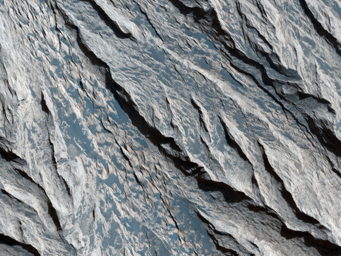Mineralische Schichten in Candor Chasma. Diese Aufnahme zeigt eine Felsklippe im Valles Marineris. Wind-Erosion hat scharfe, V-förmige Muster in die Schichten eingeprägt.